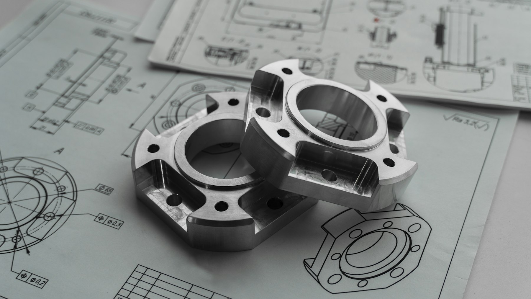 Teknik çizimlerin üzerinde duran işlenmiş metal parçalar